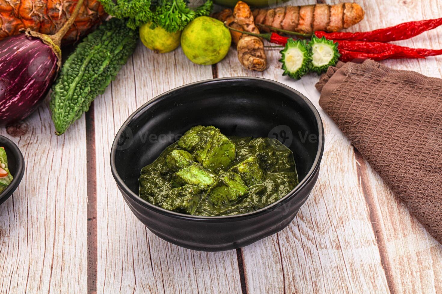 A bowl of green food sitting on a table next to other vegetables photo