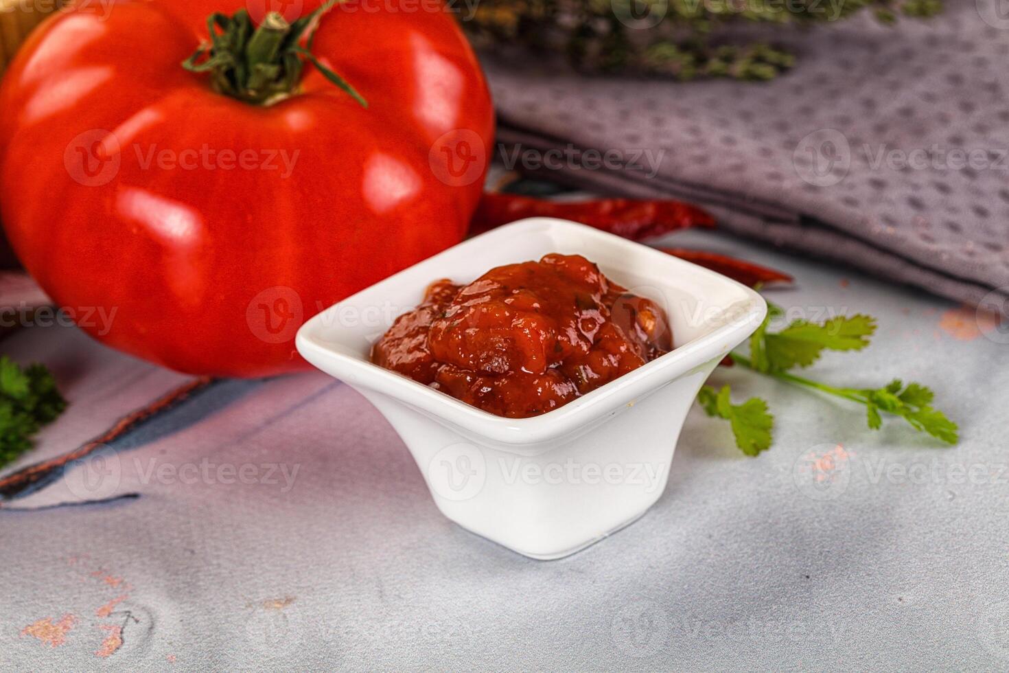 A tomato, a bowl of sauce and a bowl of vegetables photo