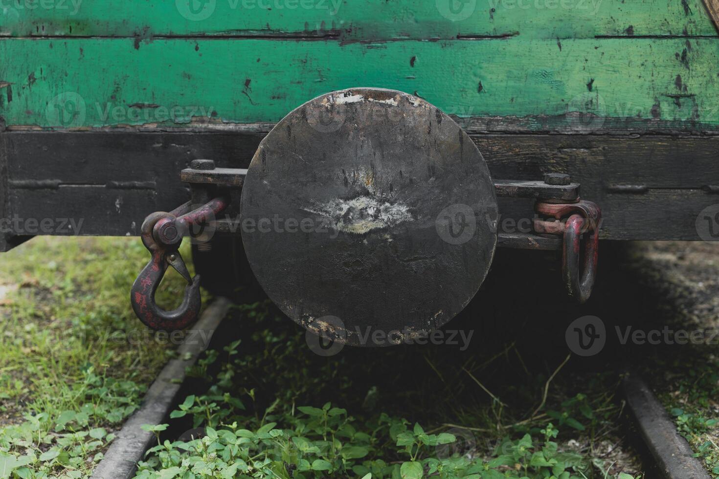 Close-up view of an antique train coupling on overgrown tracks surrounded by lush green vegetation in a forgotten railway yard photo