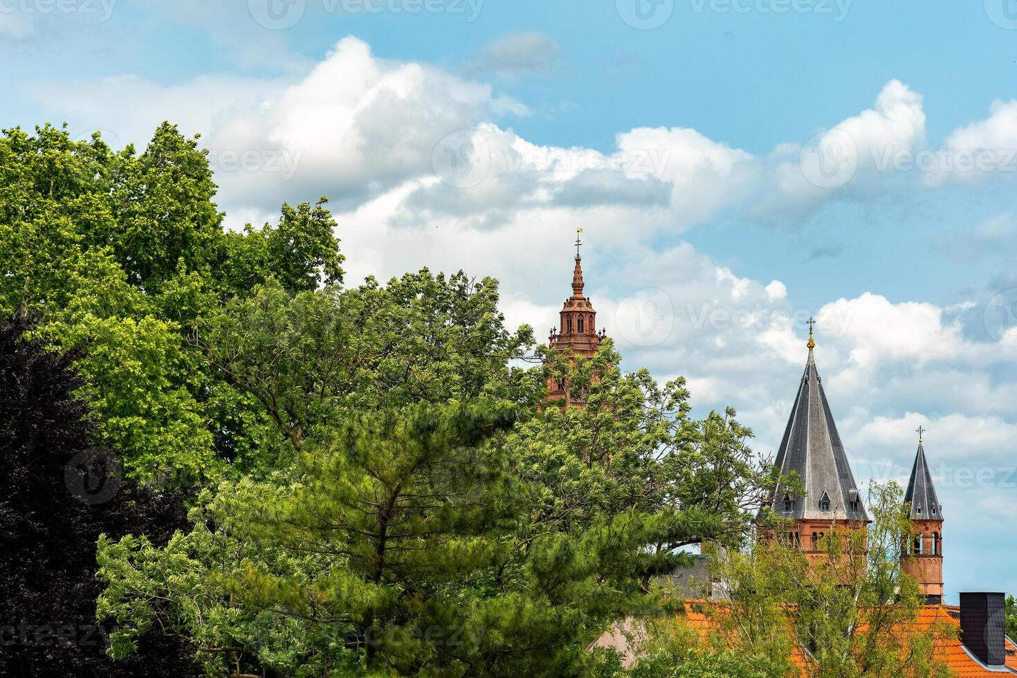 View of historic spires rising among lush greenery in a vibrant spring sky filled with soft, fluffy clouds photo