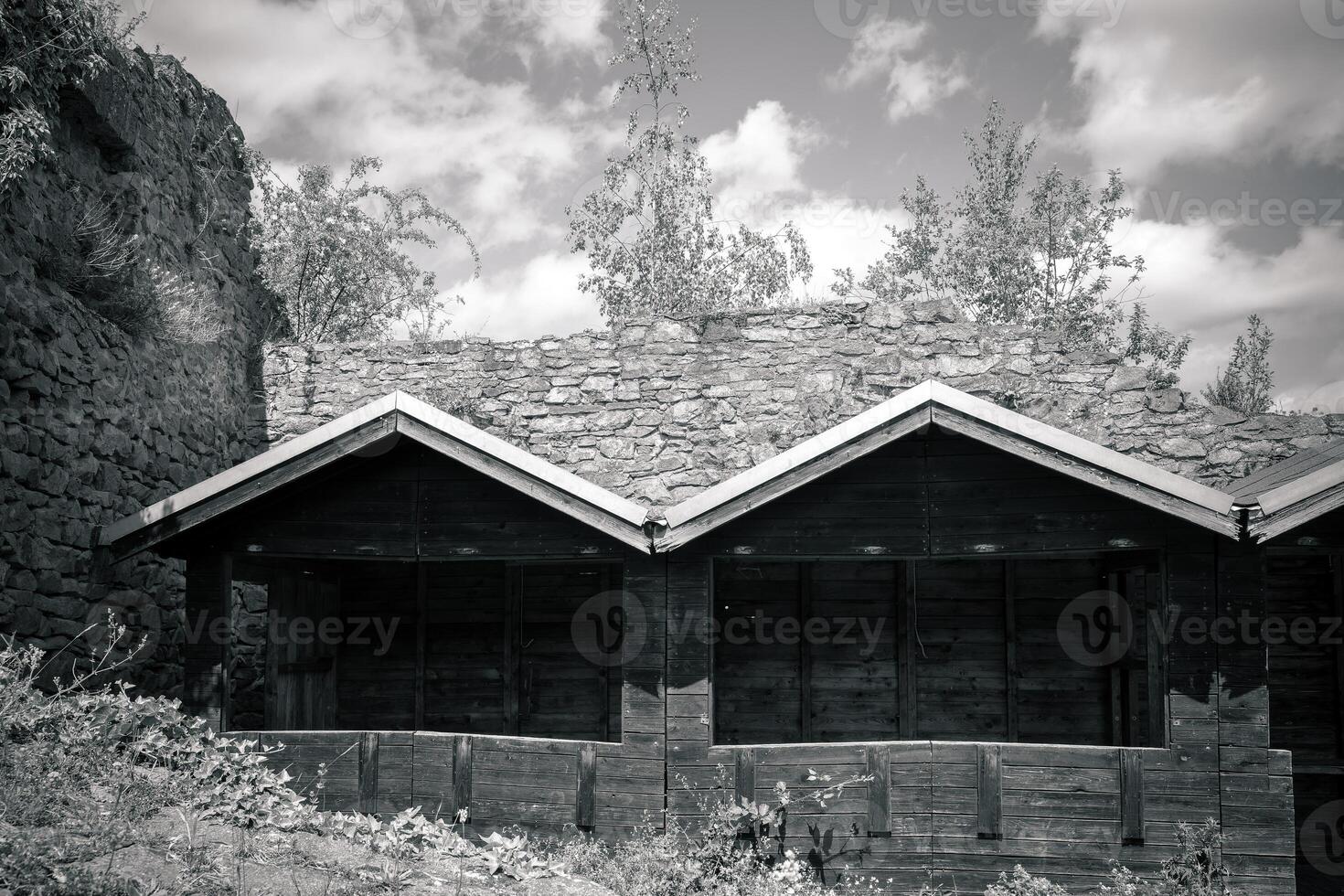 Weathered wooden structure nestled among rugged stone and verdant trees under a dramatic sky photo