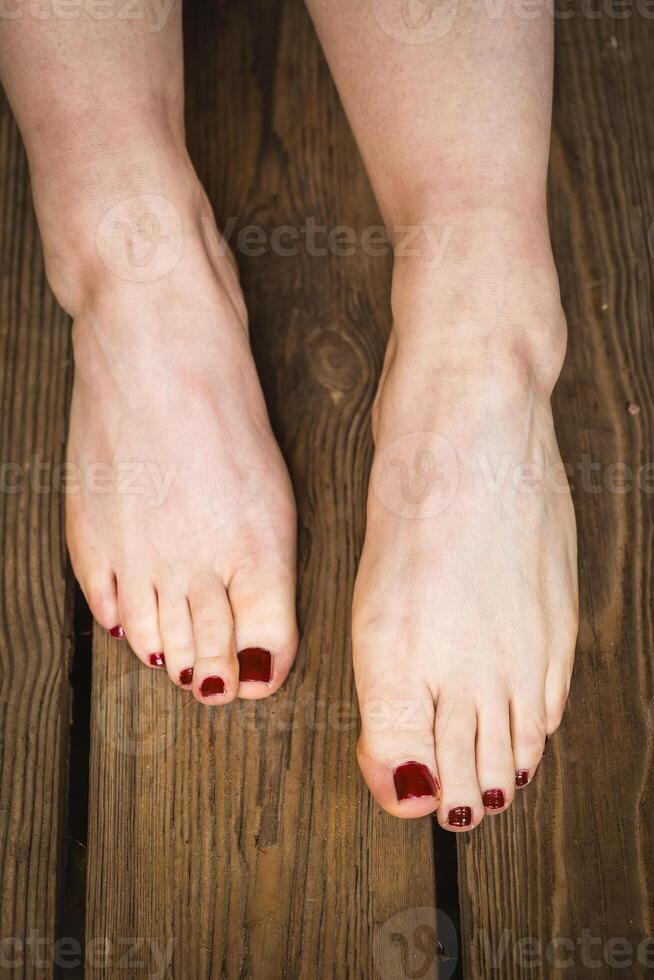 Well-manicured feet on wooden deck during sunny day showcasing red nail polish photo