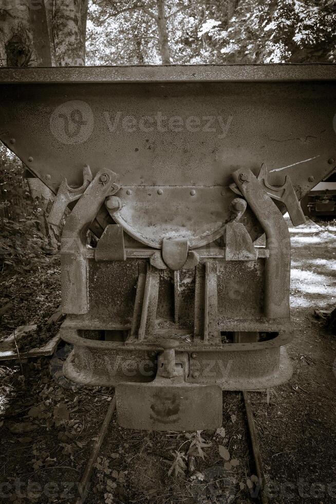 Rusty construction equipment resting in a forest setting under dappled sunlight during a warm autumn afternoon photo