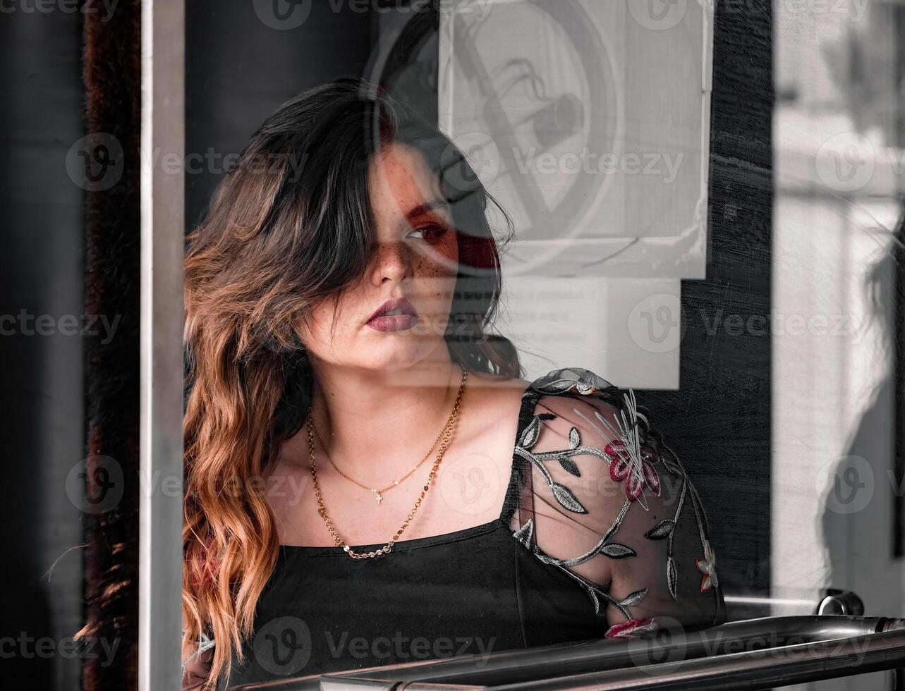Young woman gazing thoughtfully through a window in an urban setting during daylight hours photo