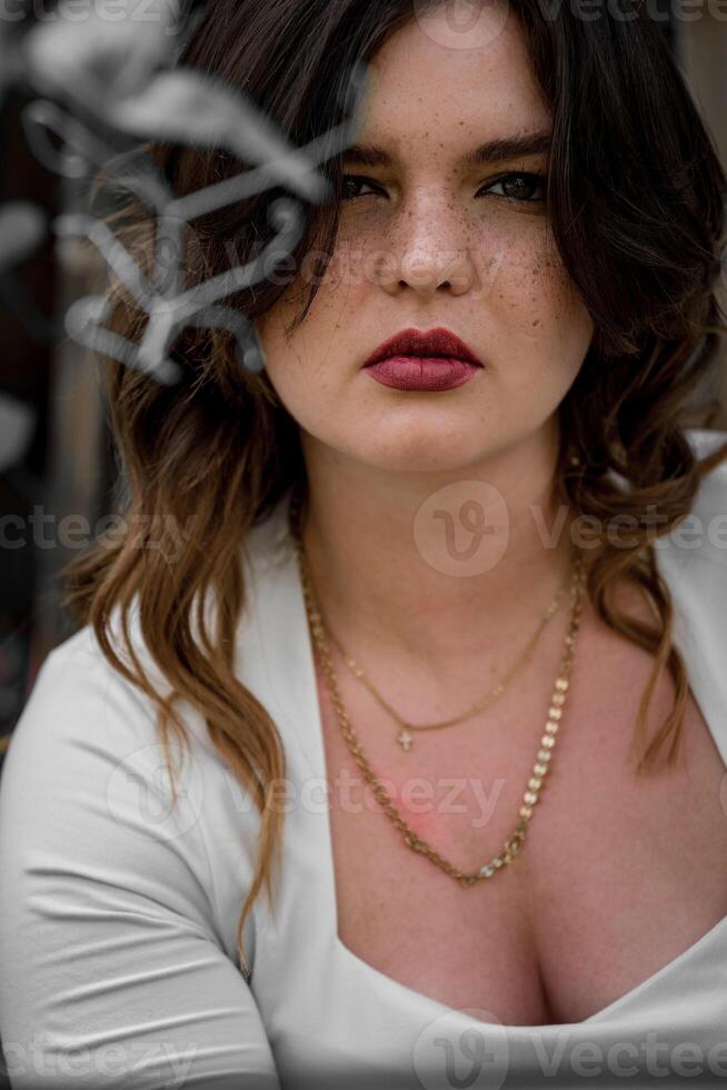 Captivating portrait of a young woman with striking features and elegant attire in an enchanting outdoor setting on a sunny day photo