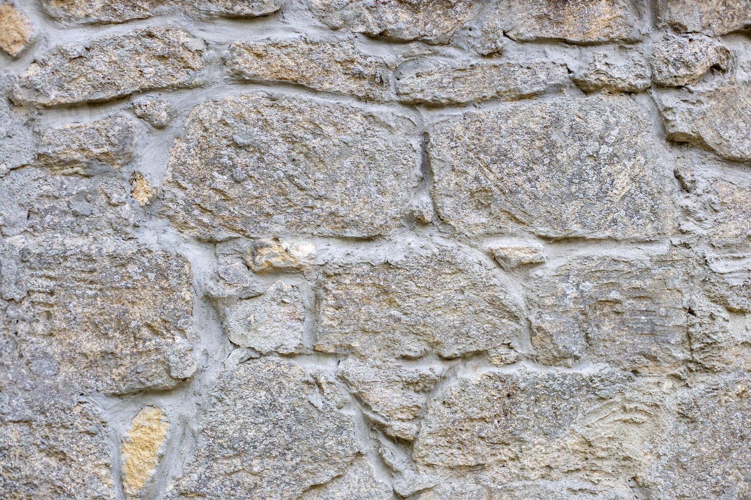 Close-up of a section of masonry with gray, uneven stones held together with cement mortar to form a textured background. photo