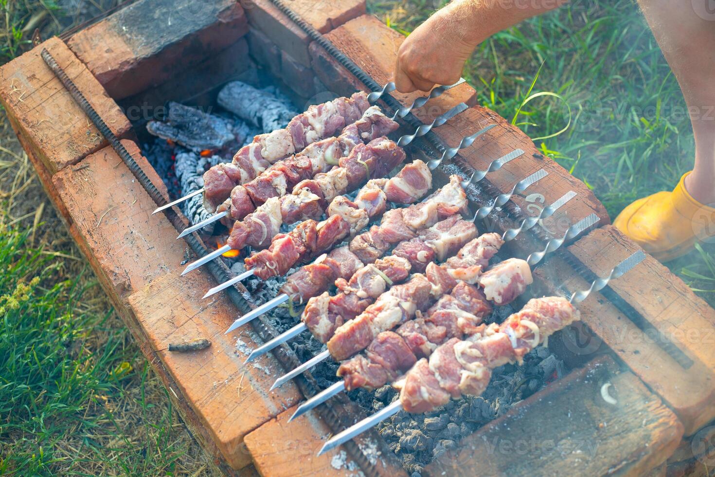 A man turns skewers of fresh pork meat on a brick barbecue in the yard of a house. Outdoor picnic with grilled shashlik. photo