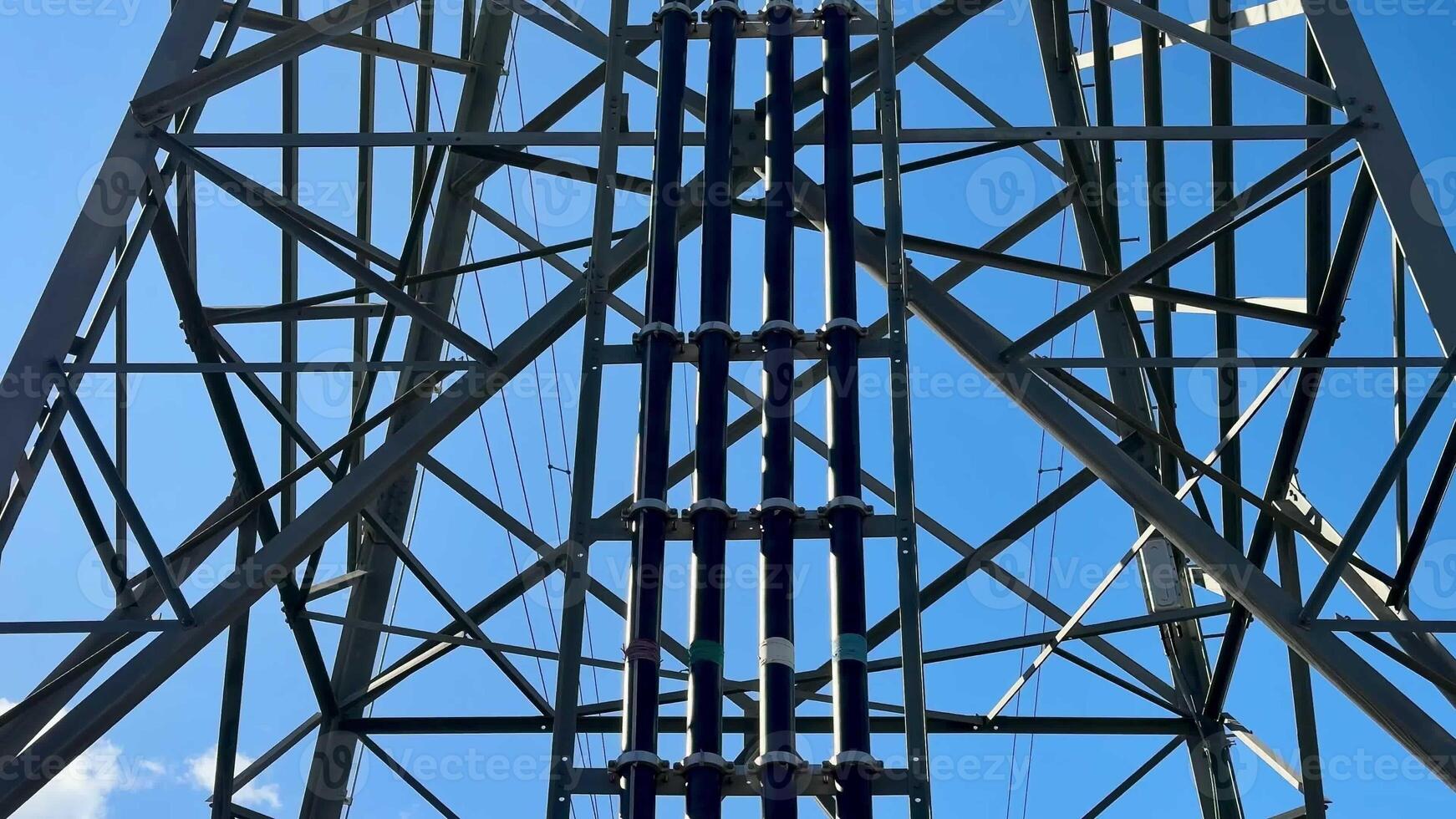 This image presents a detailed view of a high voltage transmission tower set against a clear blue sky background photo