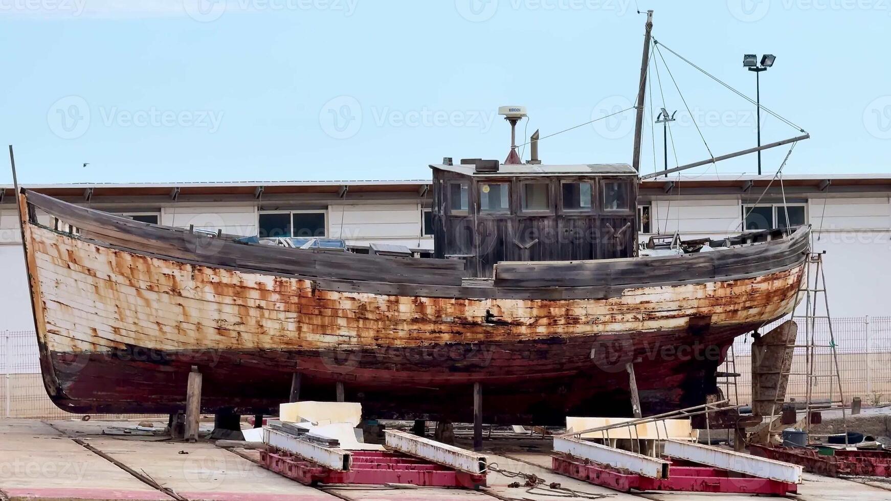 An old, weathered fishing boat, displaying visible signs of rust and decay, is currently resting in a dry dock area photo