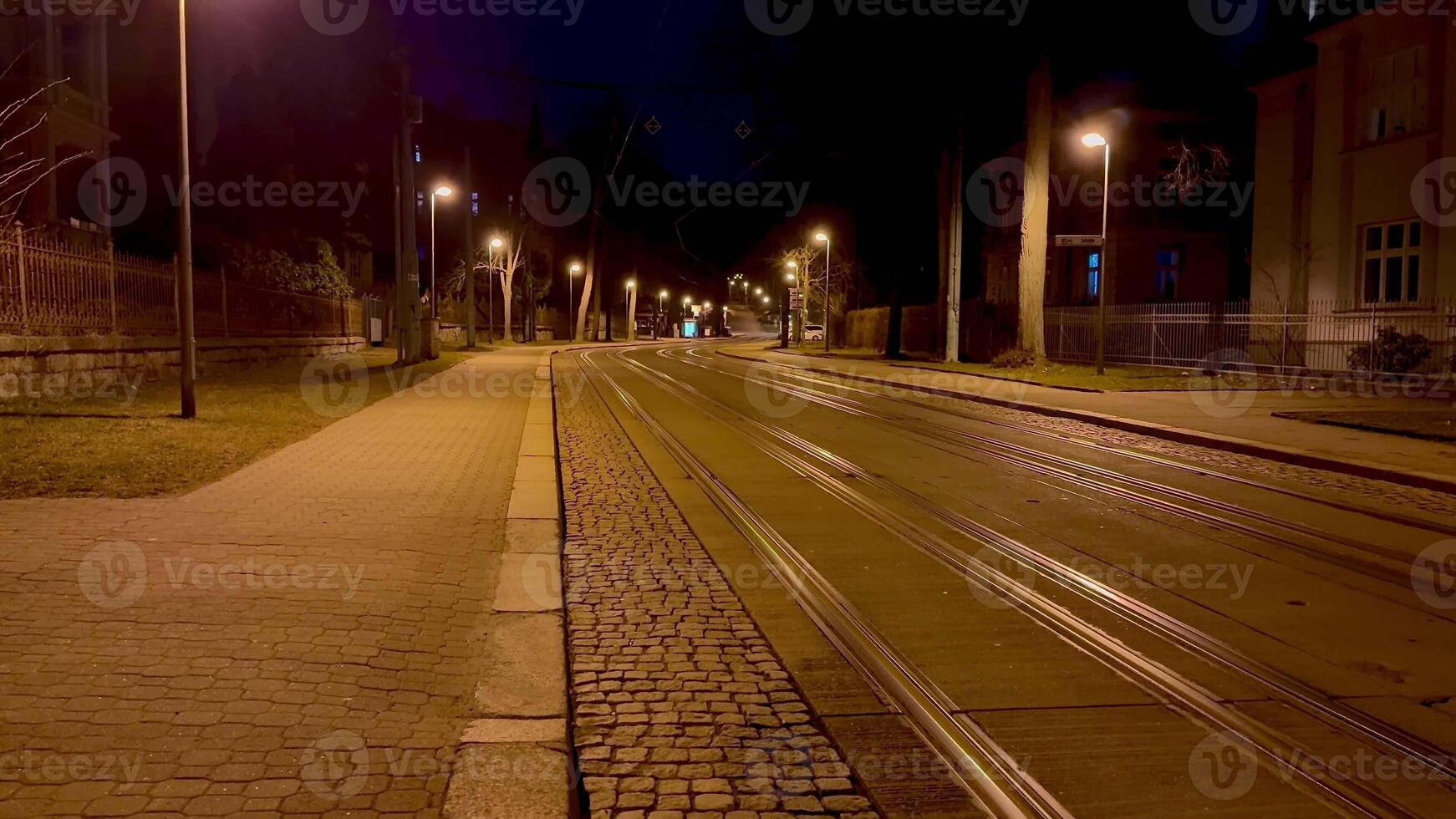 A peaceful and serene view of an empty urban street featuring tram tracks illuminated by streetlights at night photo