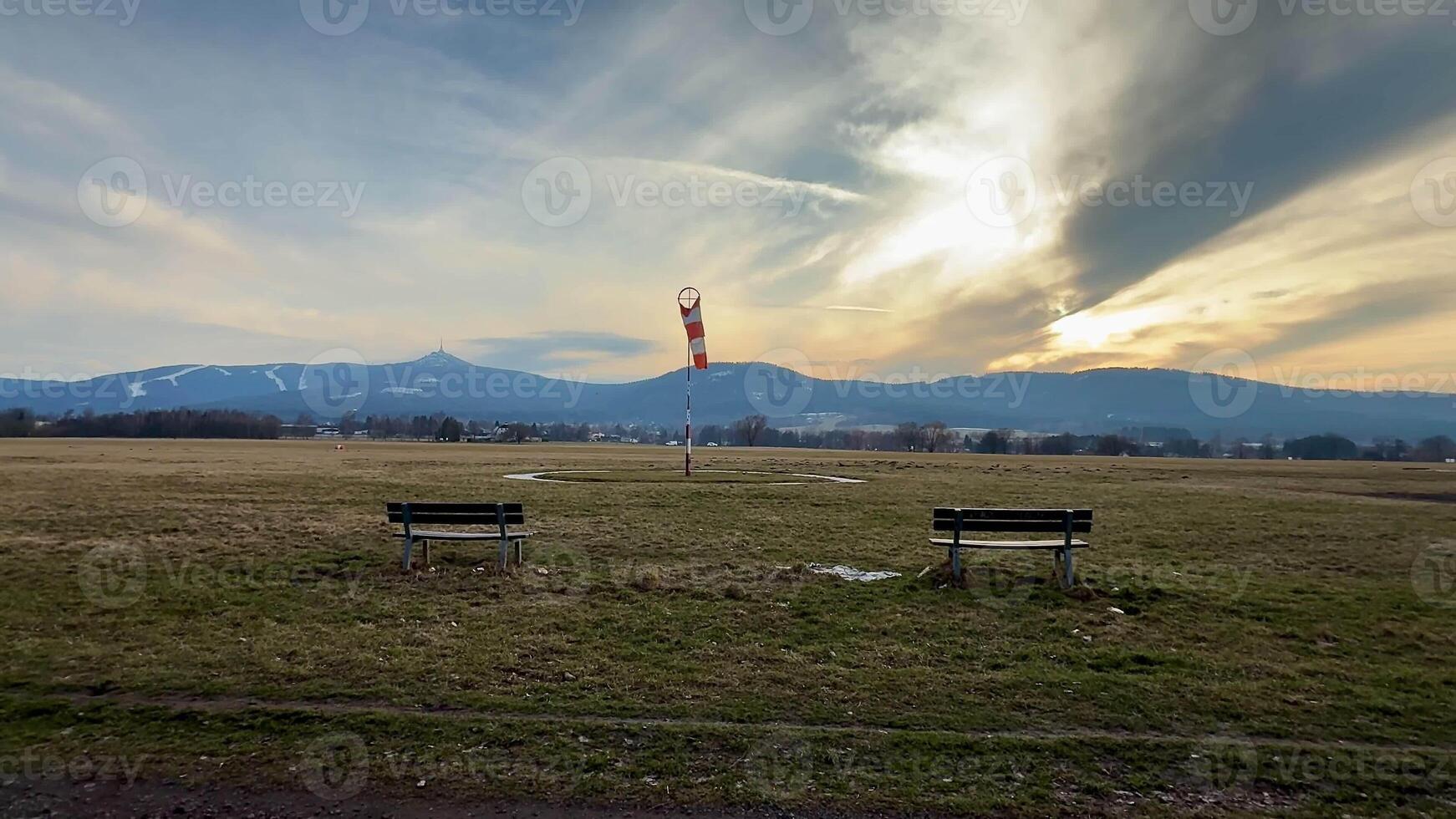 A tranquil and picturesque scene showcasing benches, expansive open fields, and majestic mountains under a stunning sky photo
