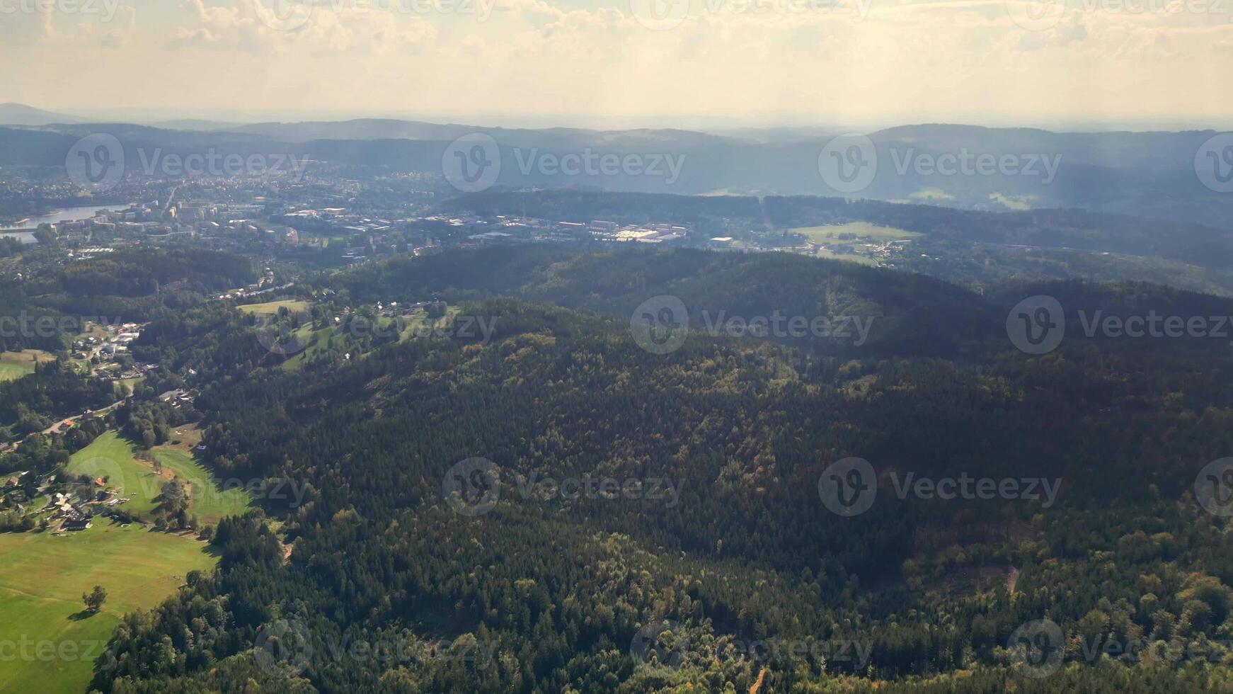 This aerial view highlights vibrant green forests and rolling hills, beautifully framed by a hazy sky photo