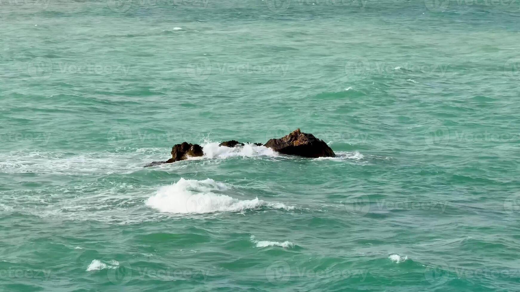 A breathtaking coastal scene featuring a rocky outcrop surrounded by turquoise waters and gentle waves. photo