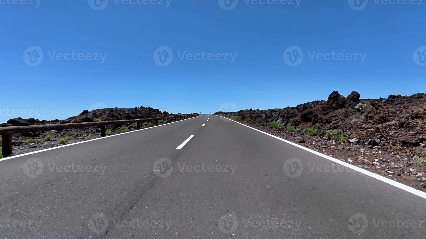 A mesmerizing view of a long highway cutting through a unique volcanic terrain under a clear blue sky. photo