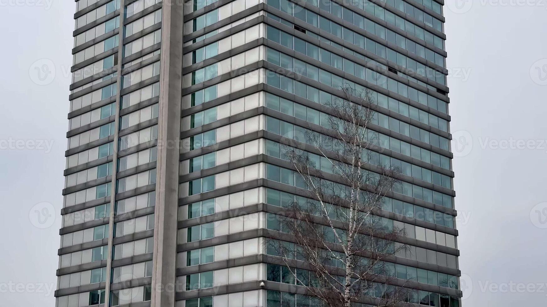 A contemporary office tower showcasing a sleek and stunning glass design positioned dramatically against a gray sky photo
