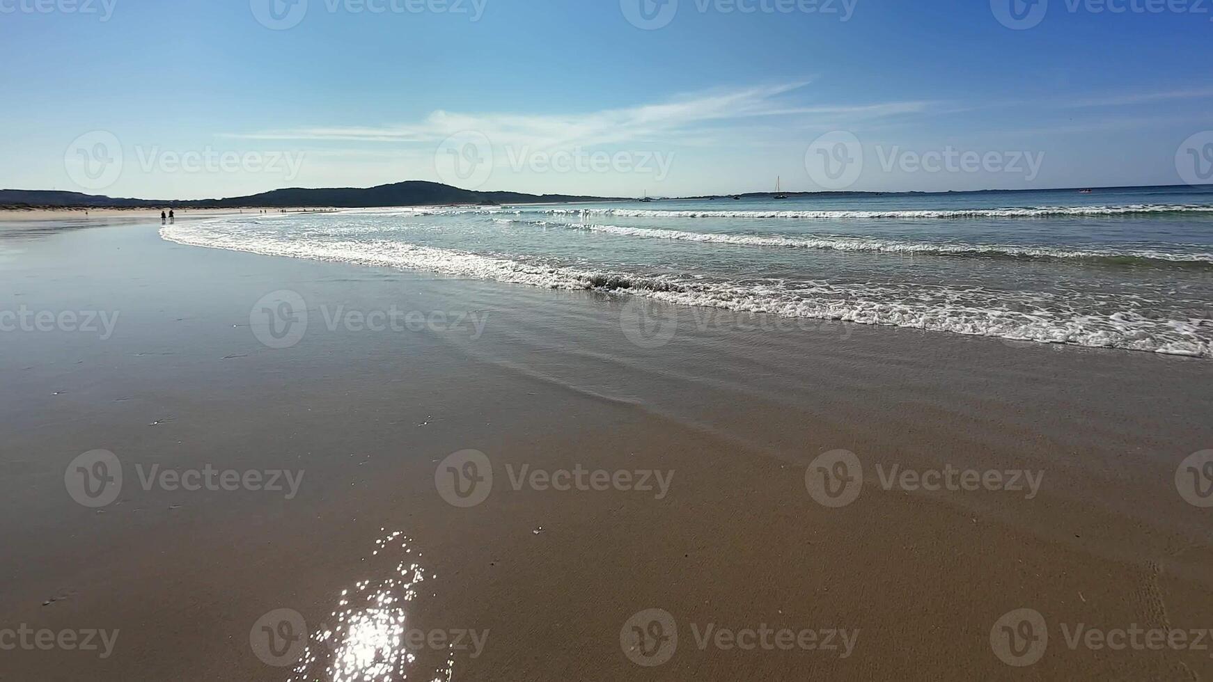 A serene beach with gentle waves lapping at the shore under a bright blue sky, perfect for relaxation photo