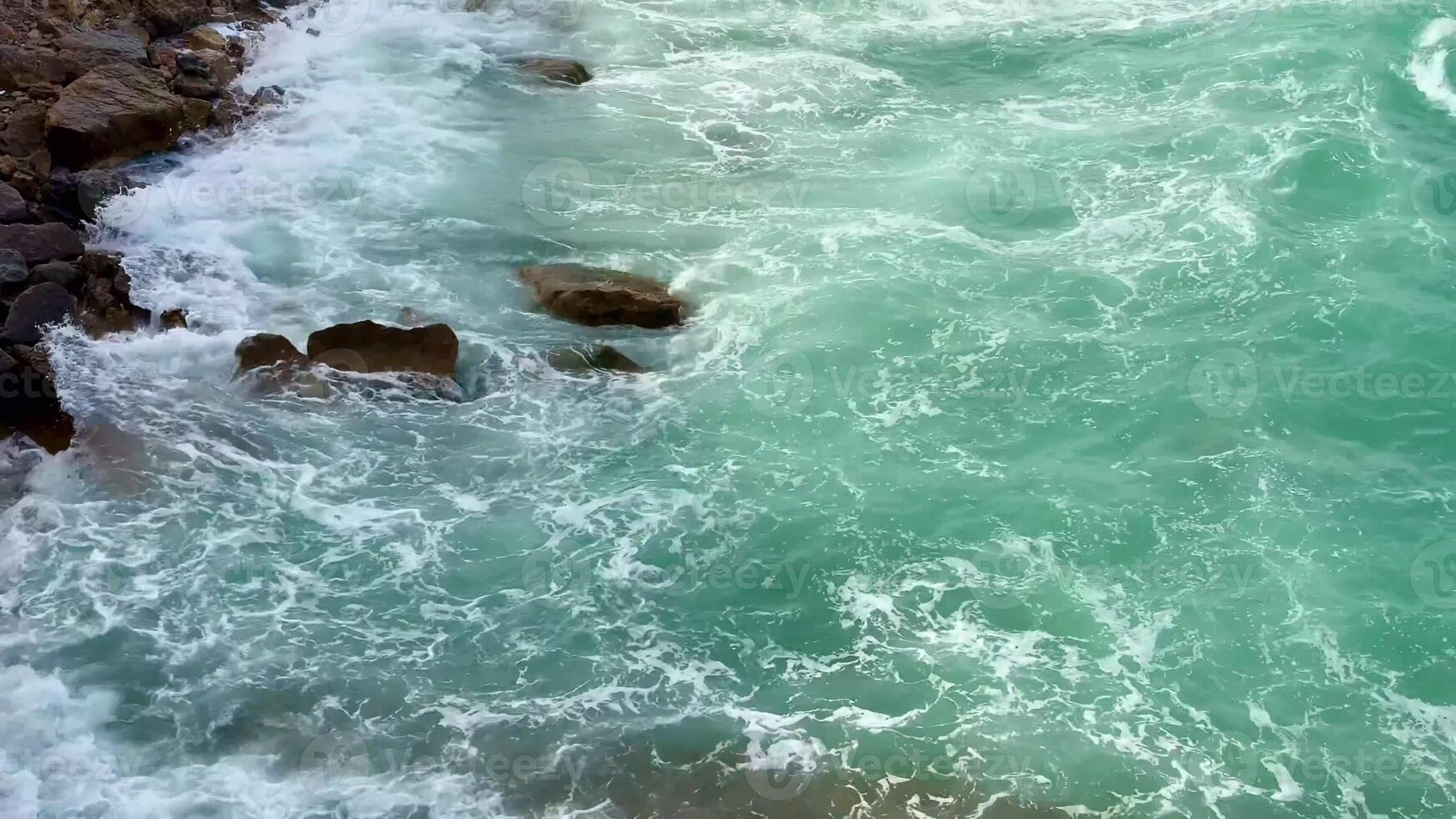 Experience the captivating and breathtaking views of turquoise waves gently washing over rugged stones along the coast photo