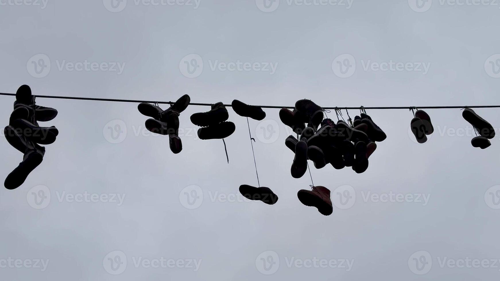 An artistic and creative display of various shoes hanging on a wire, beautifully set against a cloudy backdrop photo