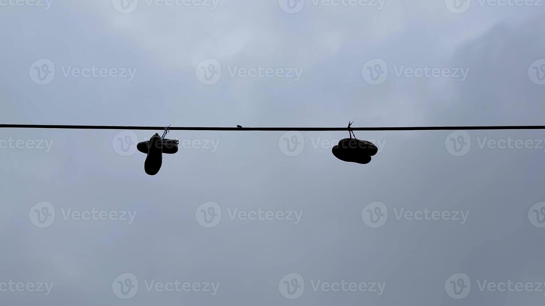 A unique pair of shoes hangs on a power line against a dramatic cloudy sky, capturing urban culture and community photo