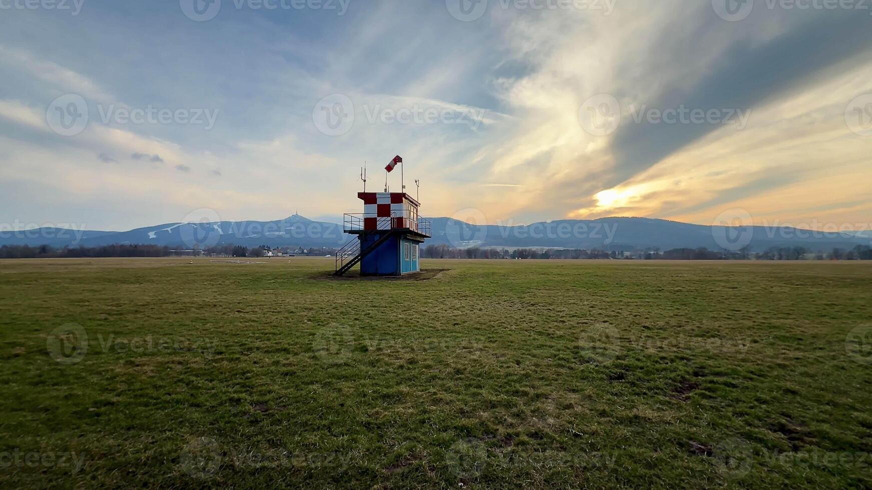 A charming lookout tower gracefully stands against a vibrant and colorful sunset in a peaceful, grassy landscape photo