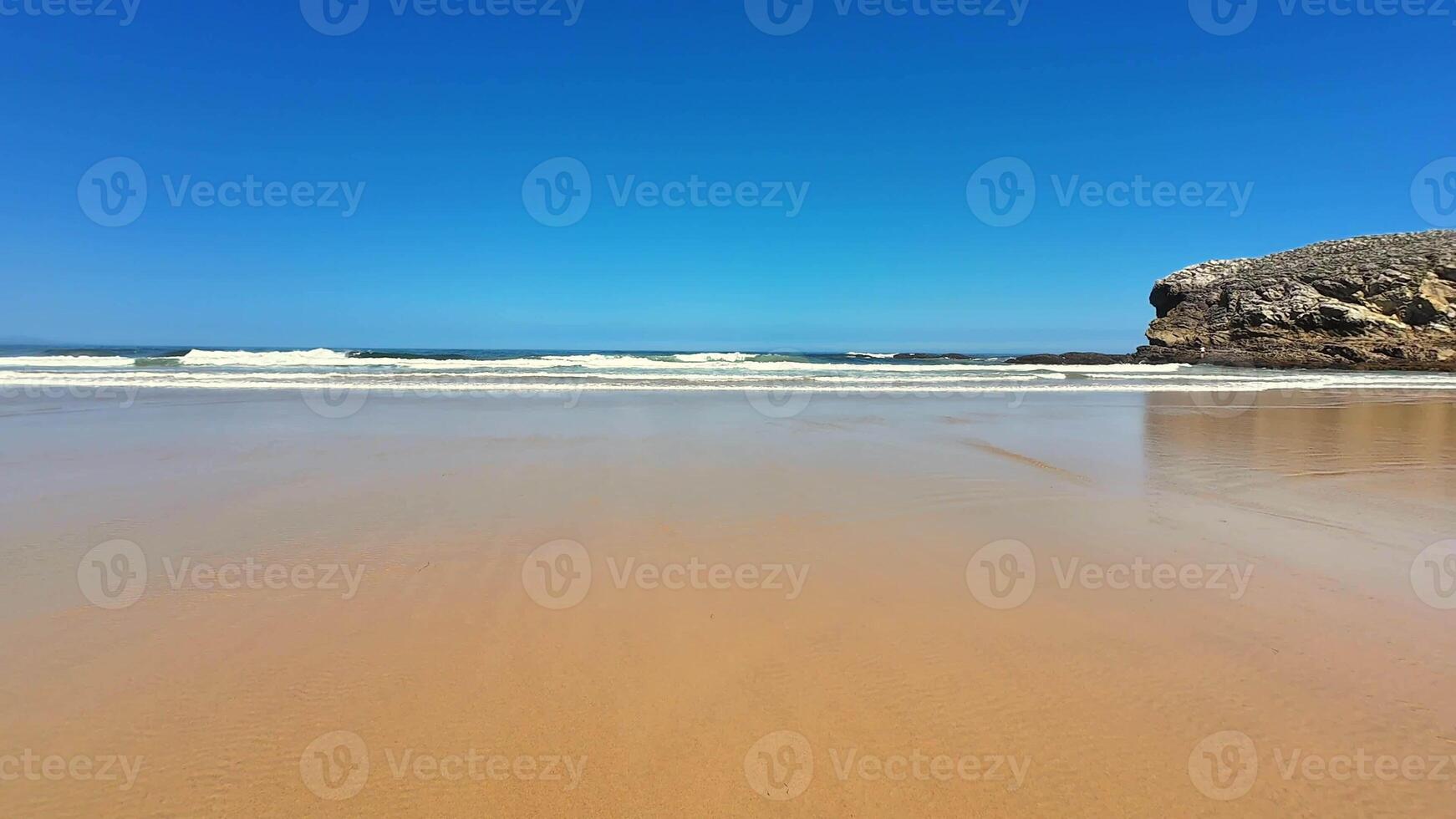 A peaceful and tranquil beach scene depicting gentle waves lapping at the shore and a clear blue sky above photo