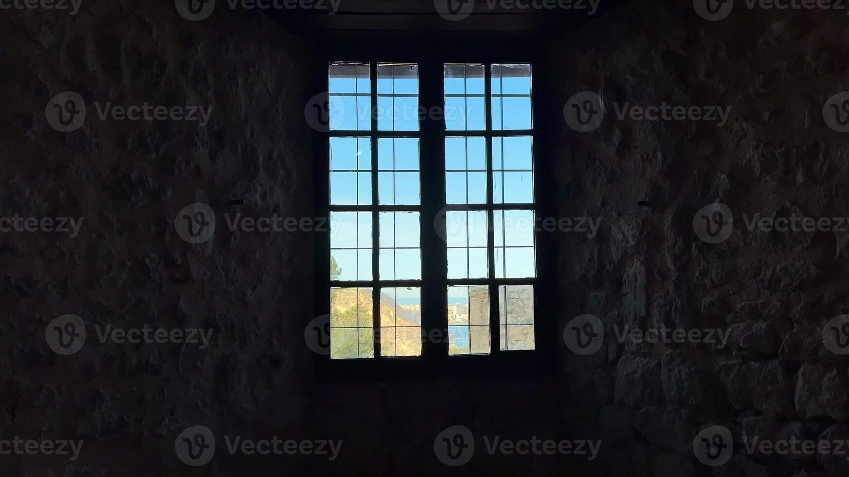A beautifully crafted window frame offers a picturesque view of nature beyond a historic stone wall photo
