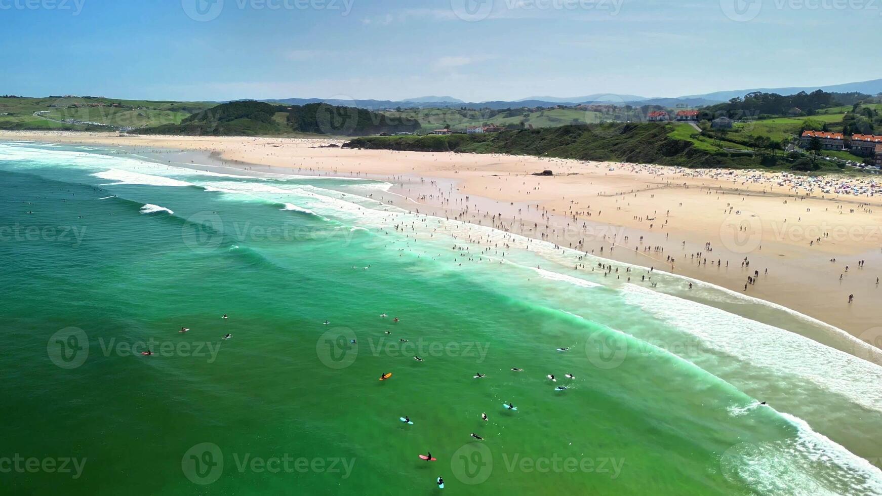 Stunning aerial shot showcasing a vibrant beach scene filled with surfers and sunbathers under clear skies. photo