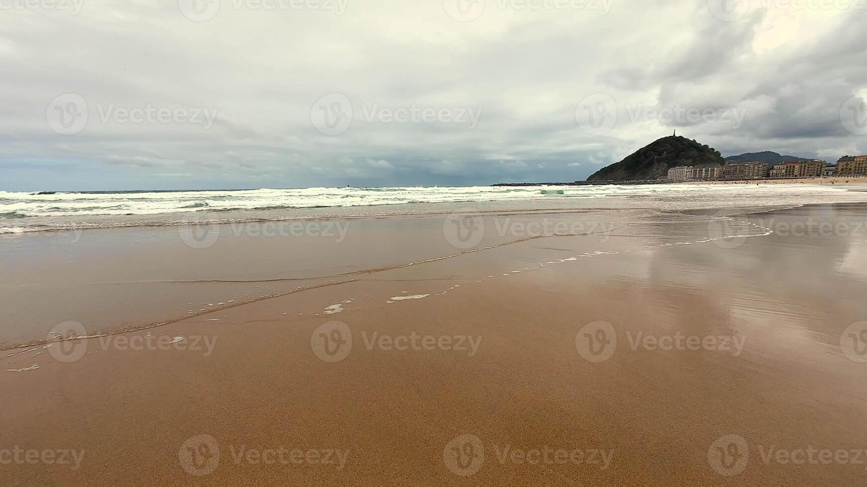 A peaceful beach scene depicting gentle waves softly lapping against the sandy shore beneath a cloudy sky photo