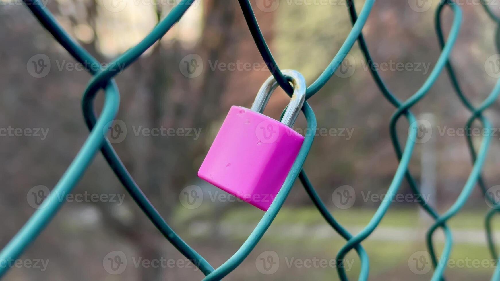 A stunning closeup shot of a vibrant bright pink padlock is hanging on a green chainlink outdoor fence photo