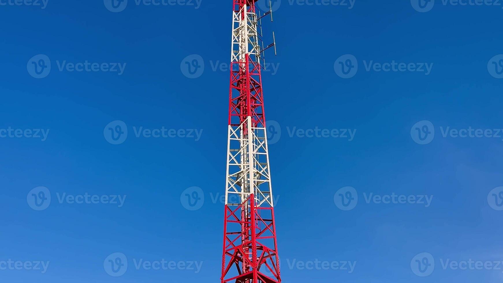 A tall communication tower featuring distinct red and white sections, beautifully set against a clear blue sky photo