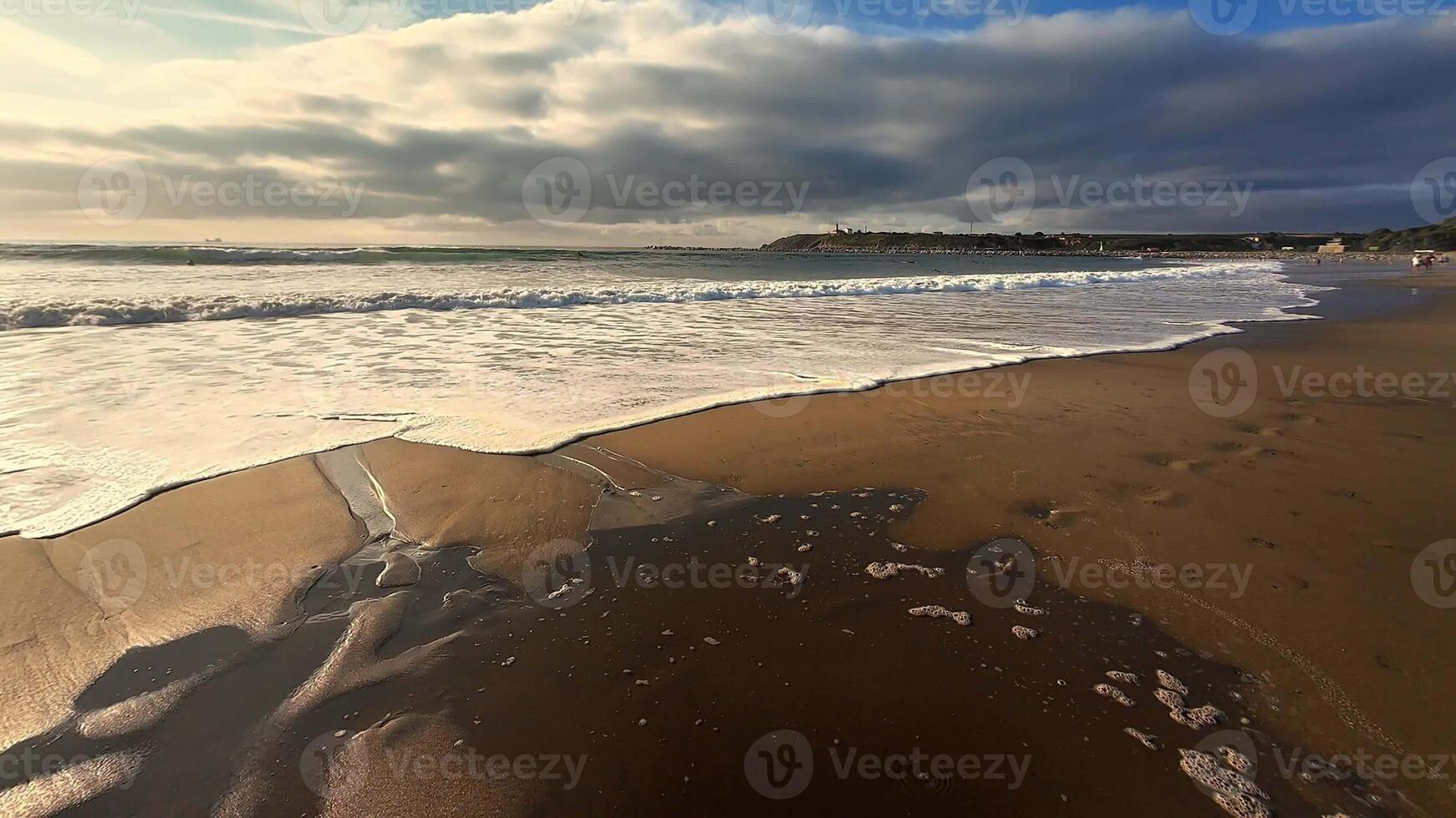 A peaceful and serene beach view showcases gentle waves, footprints on the golden sand, under a cloudy sky photo