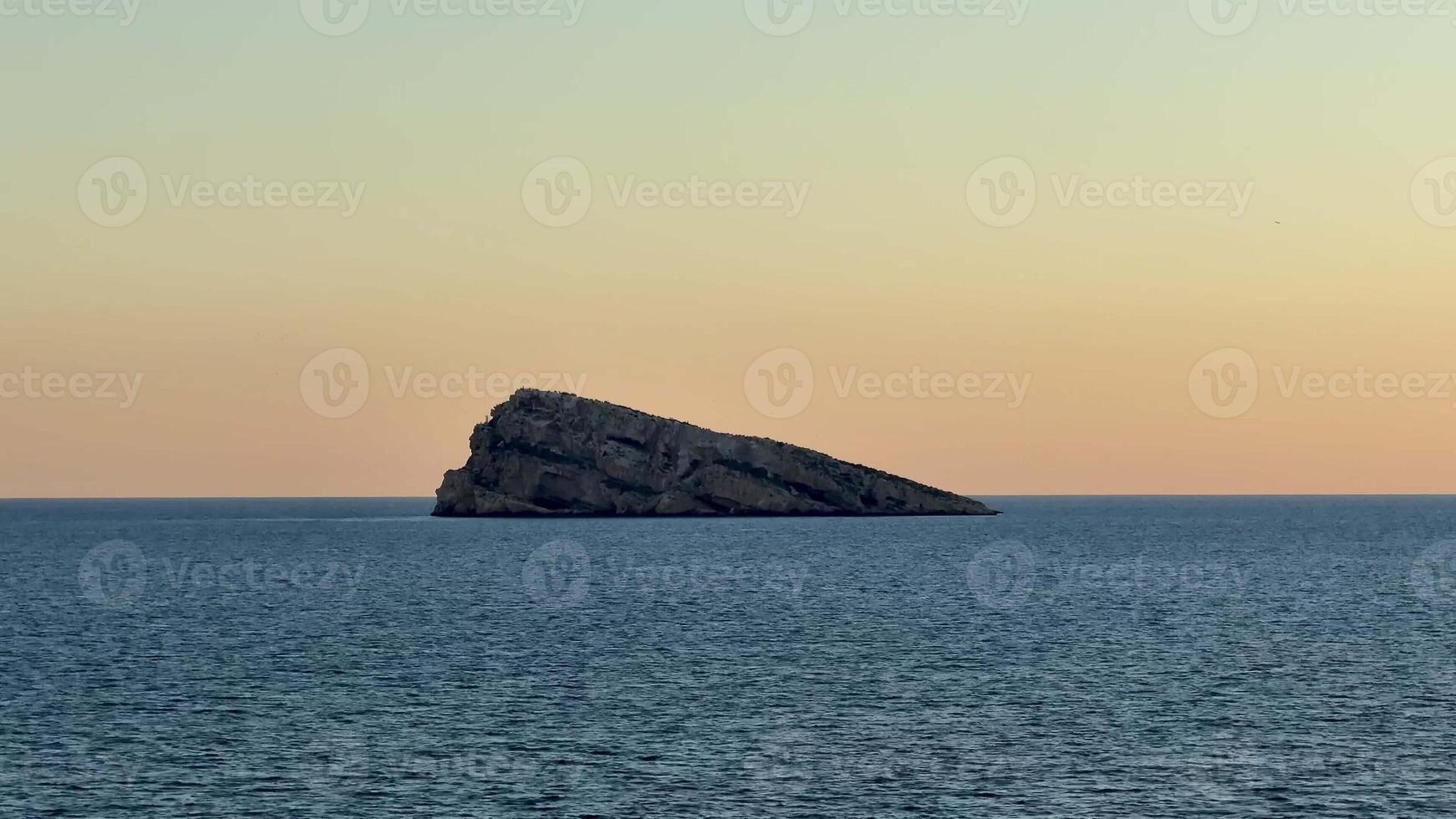 A tranquil and peaceful seascape beautifully showcasing a rocky island at picturesque sunset over serene, calm waters photo