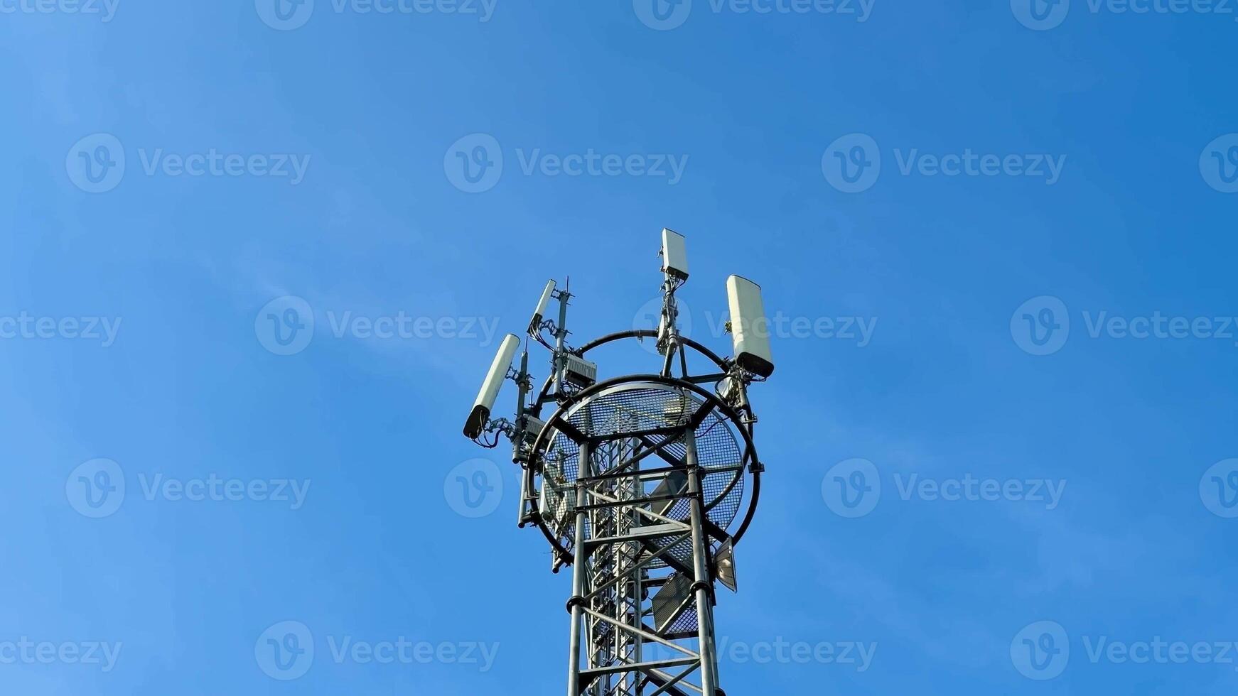 A tall communication tower with antennas looms against a blue sky, symbolizing modern technology and connectivity photo