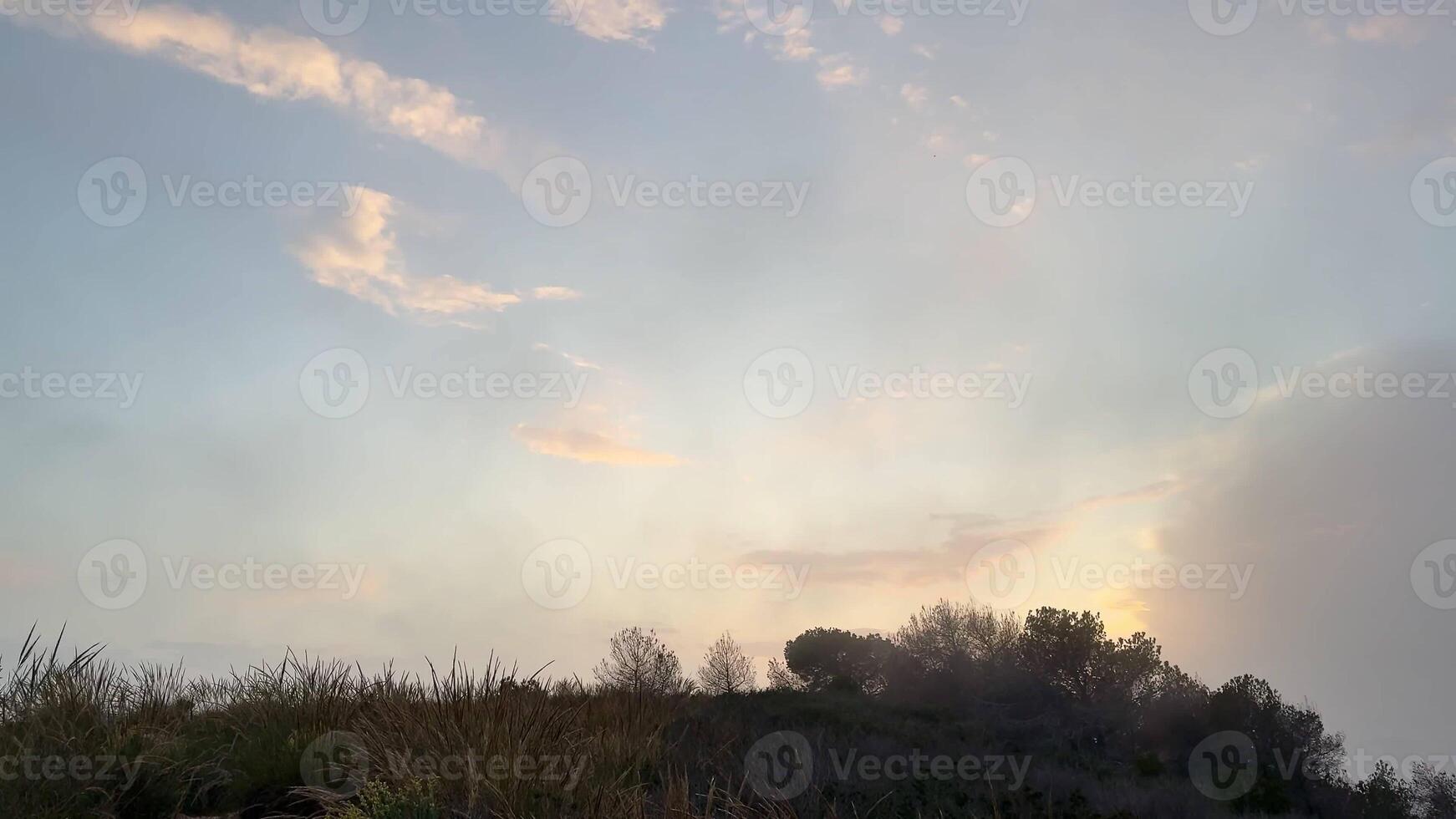 A serene view of a sunset illuminating soft clouds over rolling hills, perfect for nature-themed projects. photo