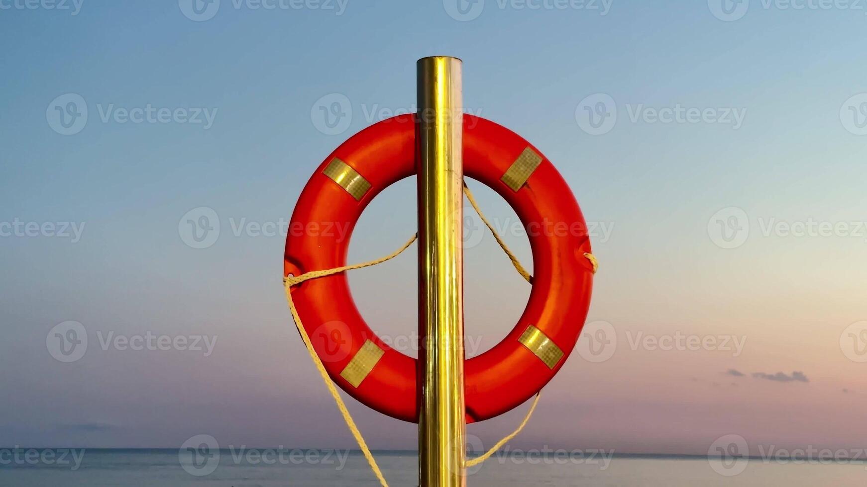 A vibrant and bright red lifebuoy stands prominently against a tranquil and serene seascape during sunset photo