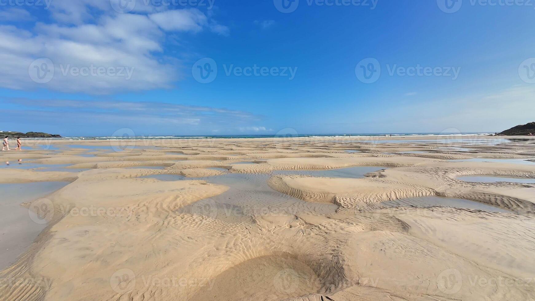 A serene and tranquil beach view showcases intricate sand patterns at low tide, all beneath a clear blue sky photo