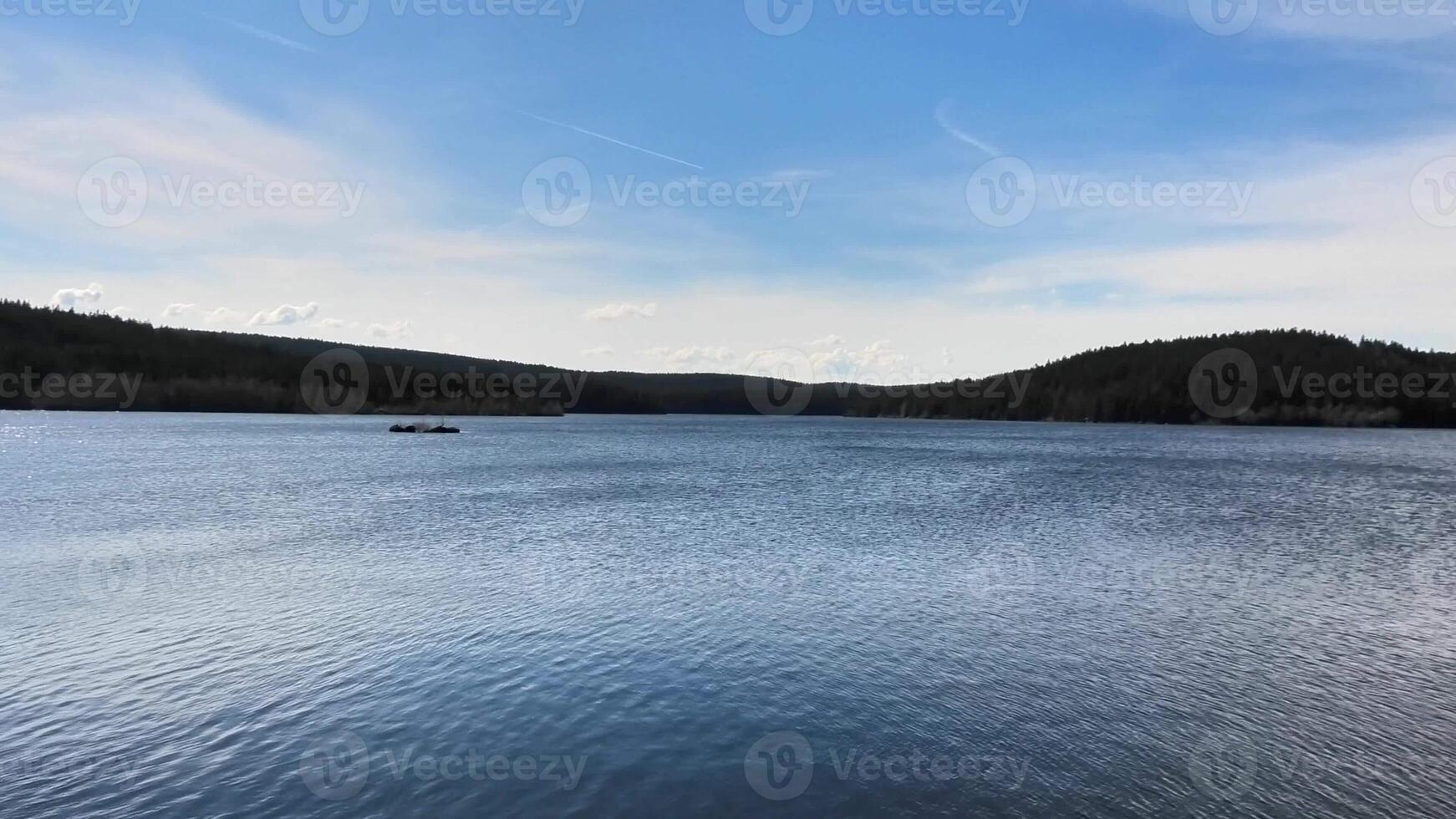 A tranquil and serene lake landscape beautifully surrounded by lush green forests beneath an expansive clear blue sky photo