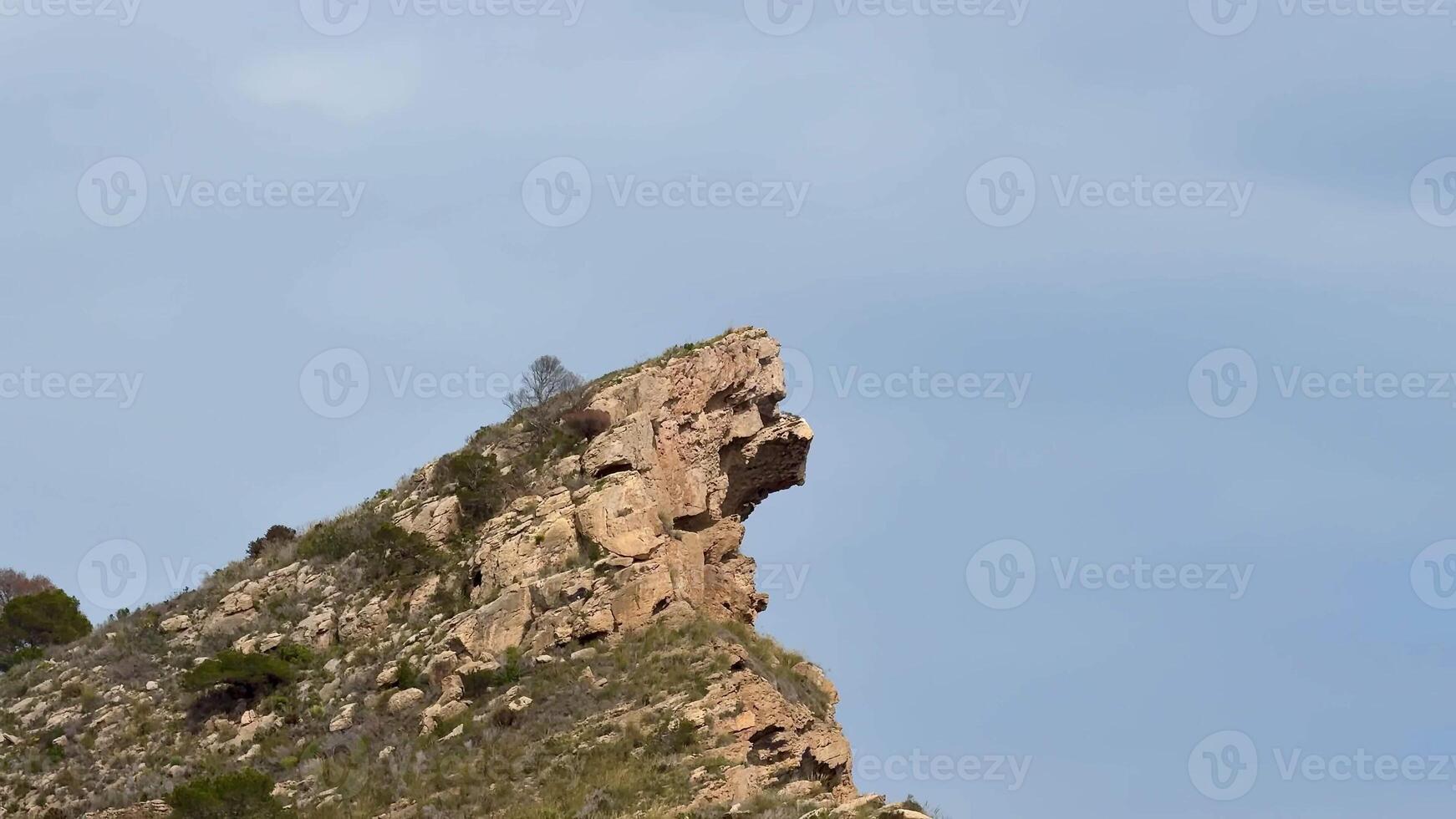 A striking rock formation resembling a human profile in a majestic mountainous landscape under a clear sky photo