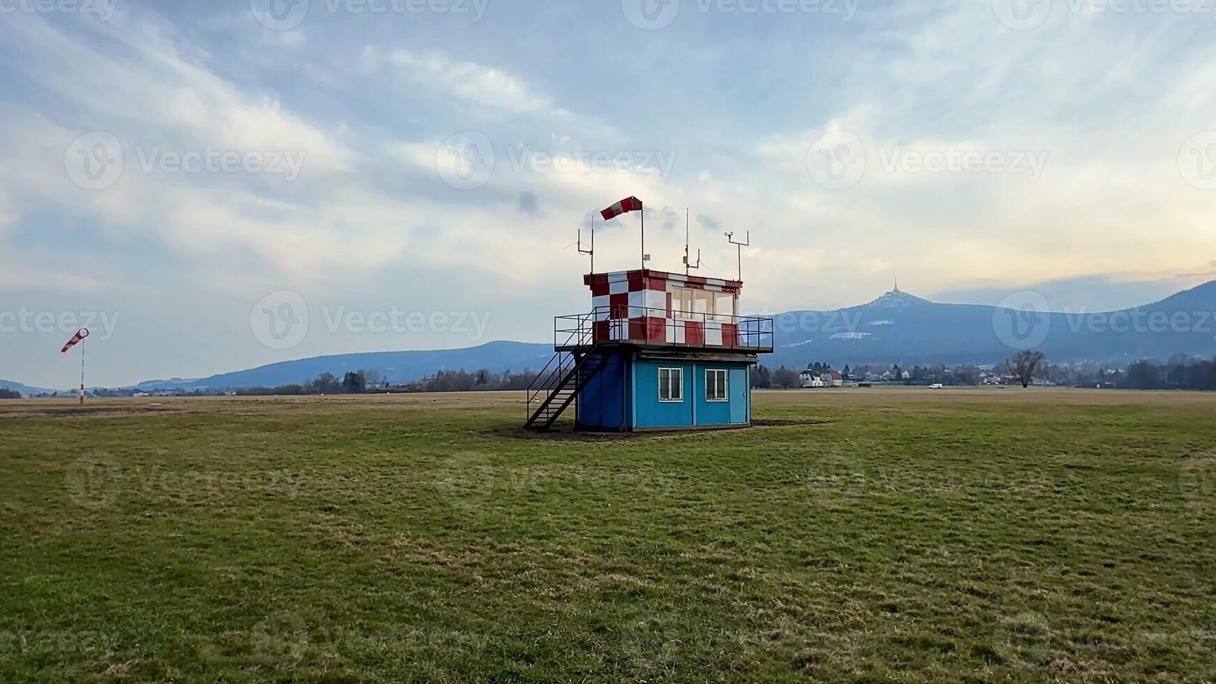A vibrant wind observation tower is surrounded by lush greenery and stunning mountains beneath a cloudy sky photo