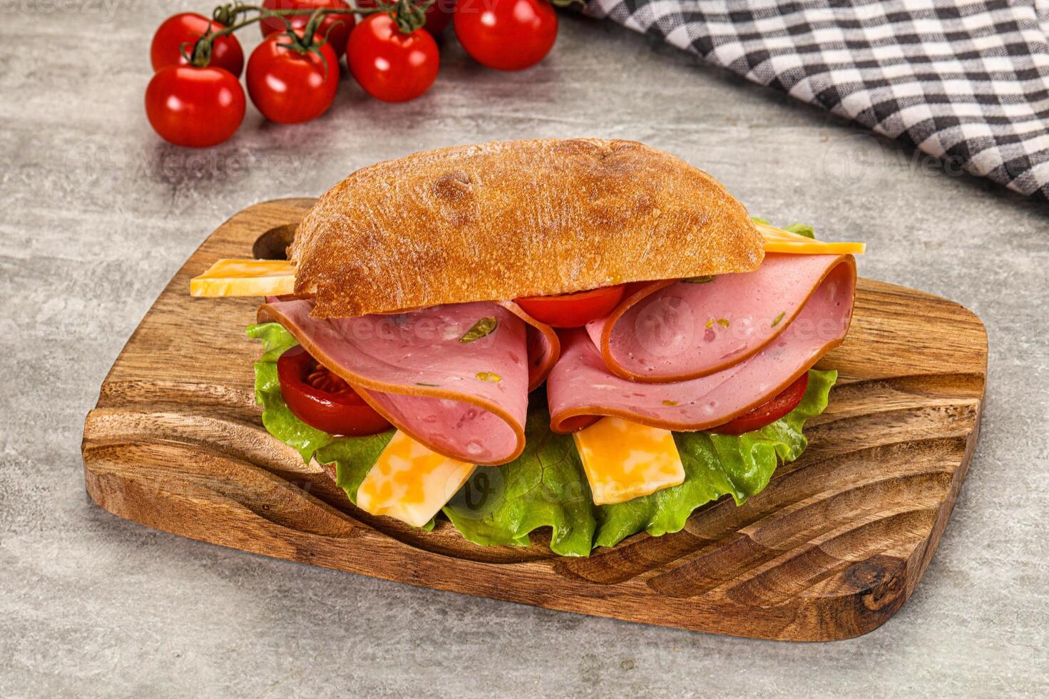A sandwich with ham, cheese, lettuce and tomatoes on a wooden cutting board photo