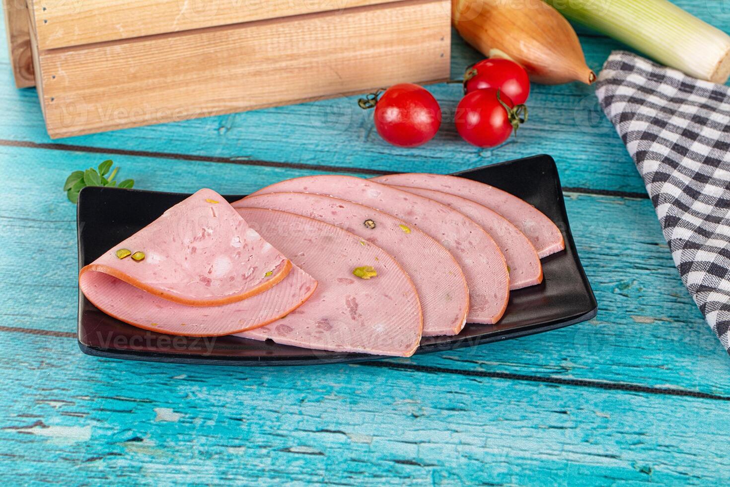 Sliced ham on a black plate with vegetables and a wooden box photo