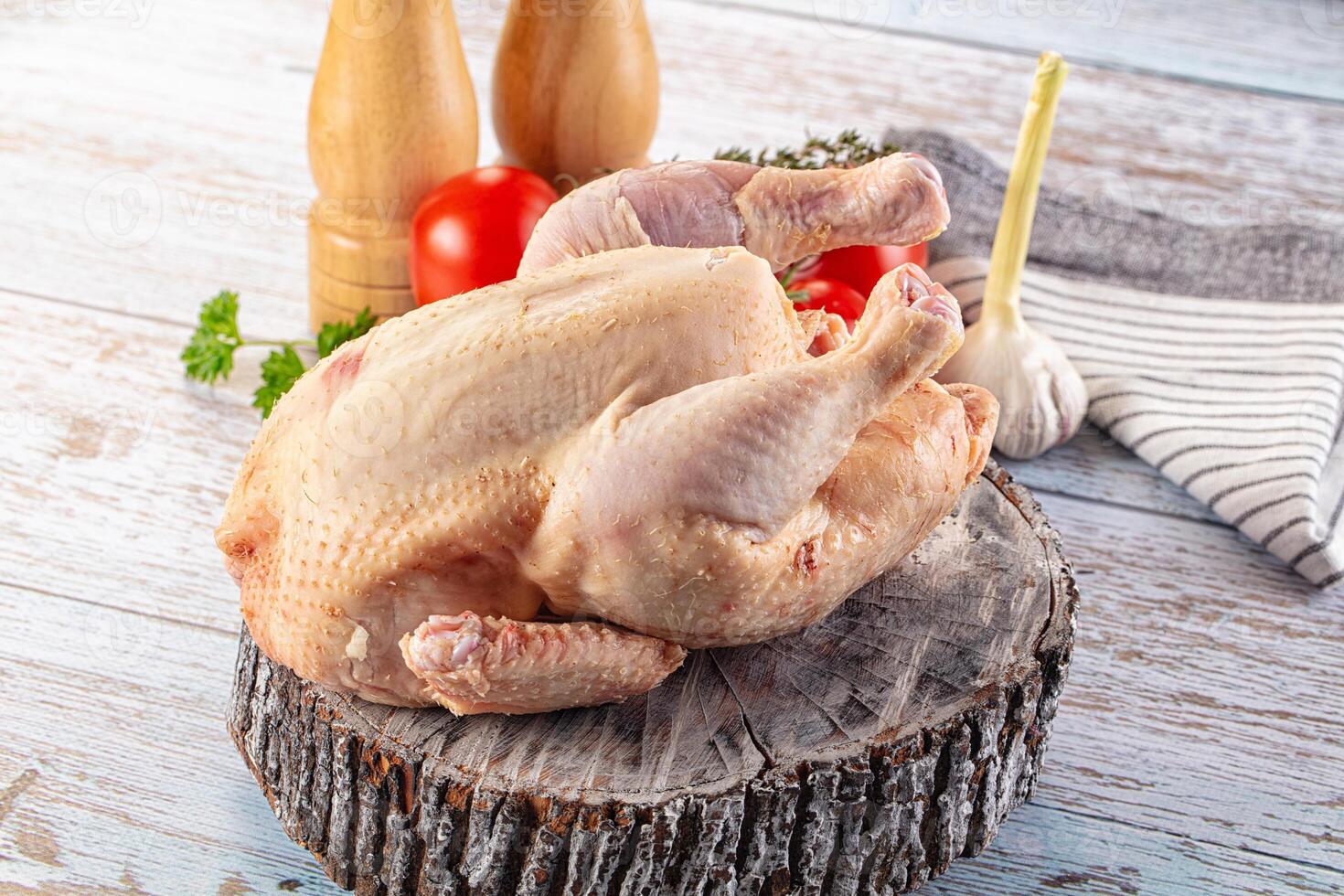 A chicken on a wooden table with a knife and a tomato photo