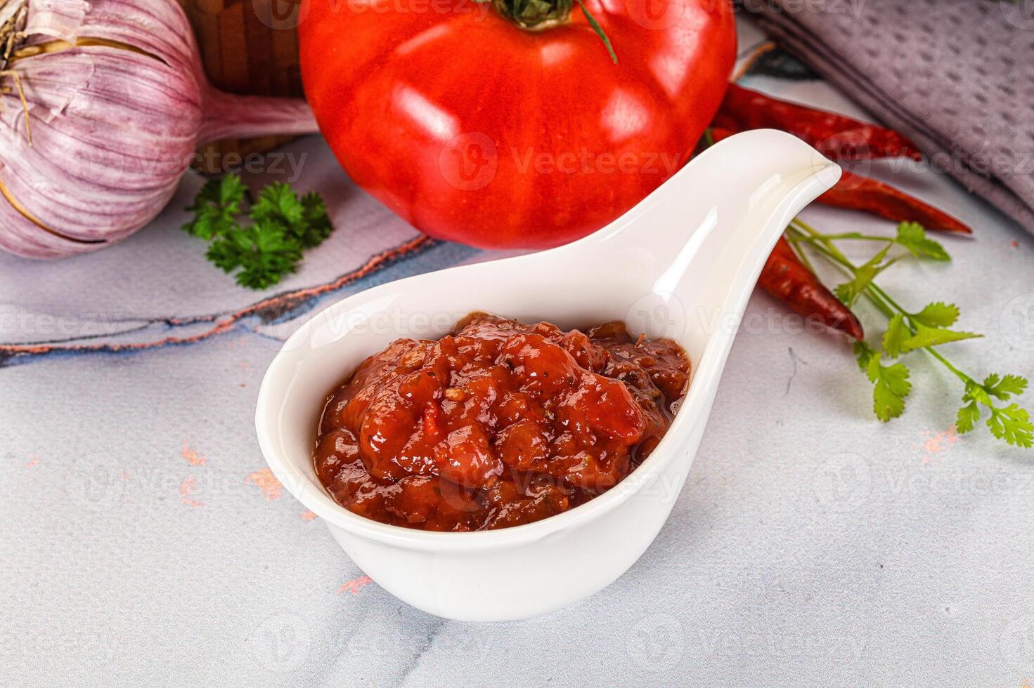 A white spoon with a small bowl of tomato sauce photo