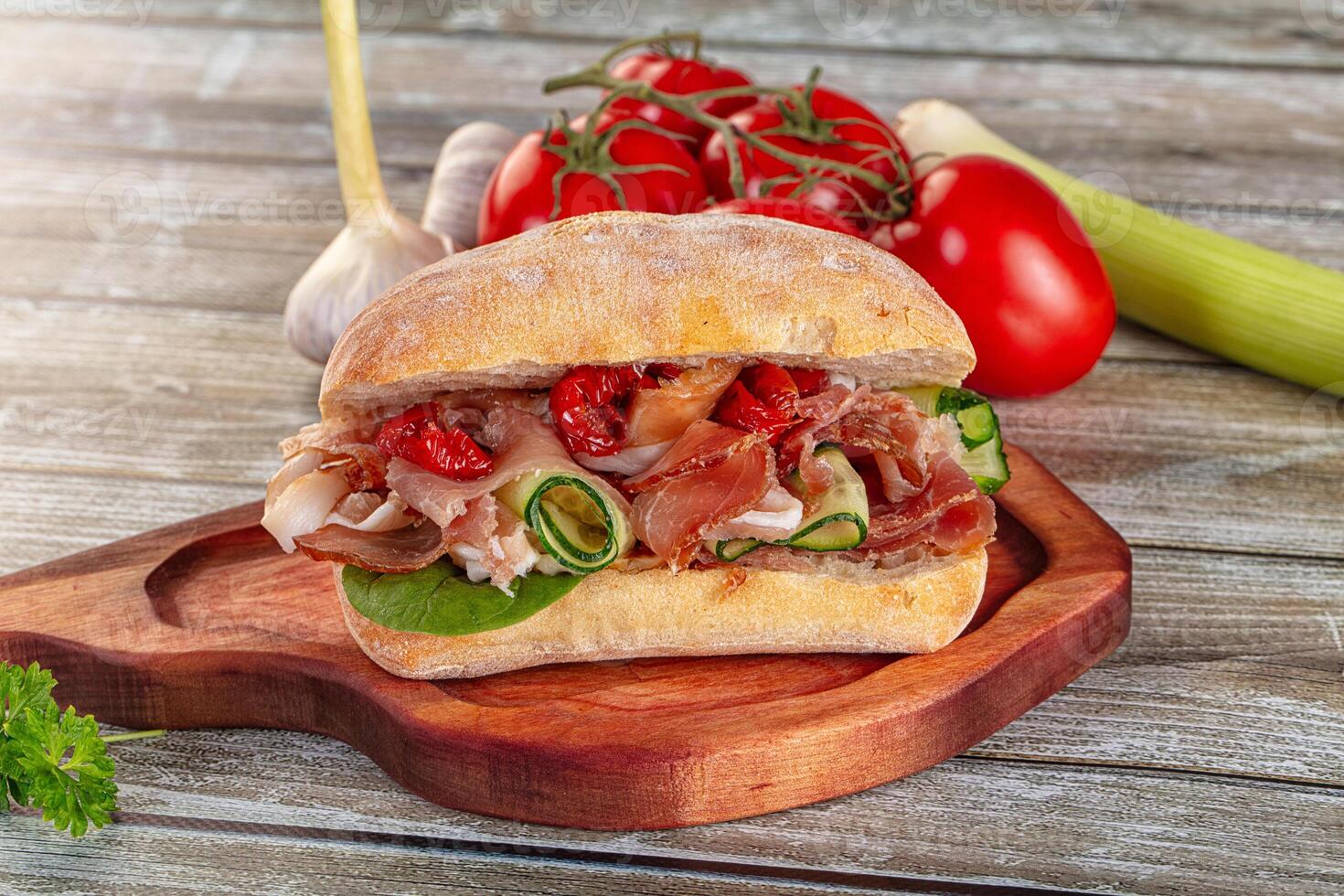 A sandwich with meat, vegetables and tomatoes on a wooden cutting board photo