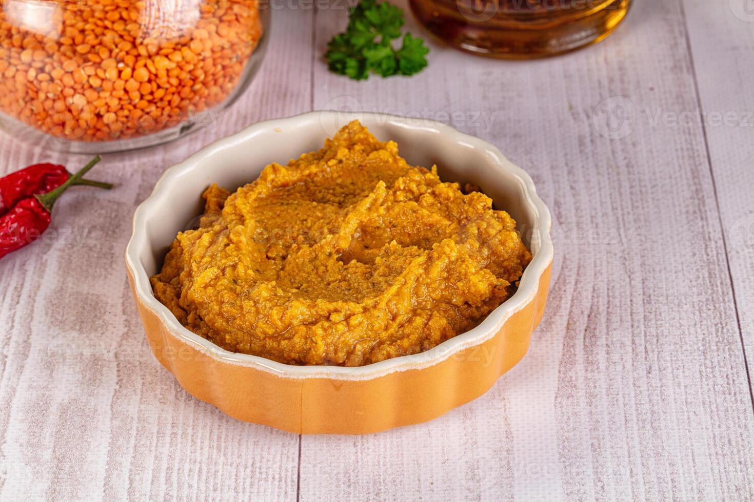 A bowl of lentil dip next to a bottle of chili photo