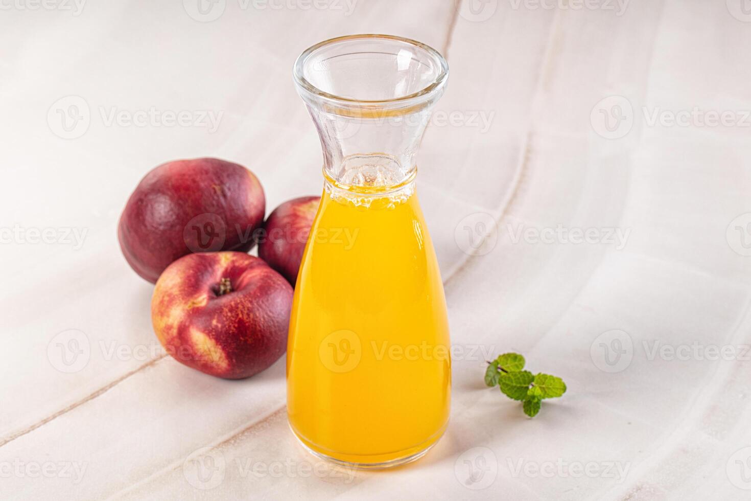 A glass jug with a glass of juice next to some peaches photo