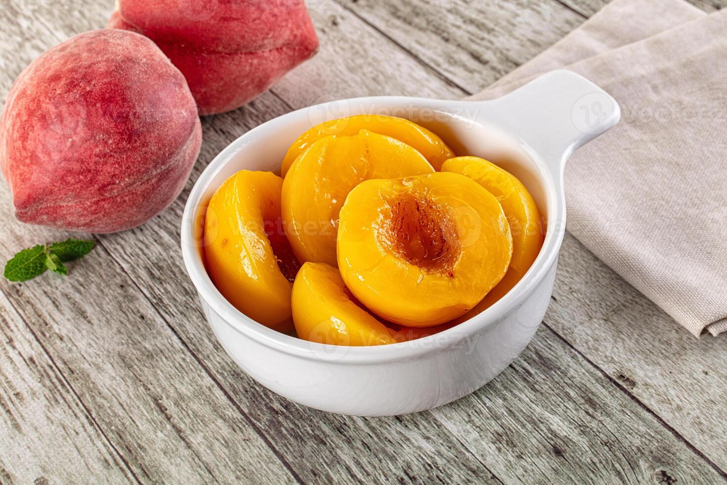 A bowl of sliced peaches on a wooden table photo