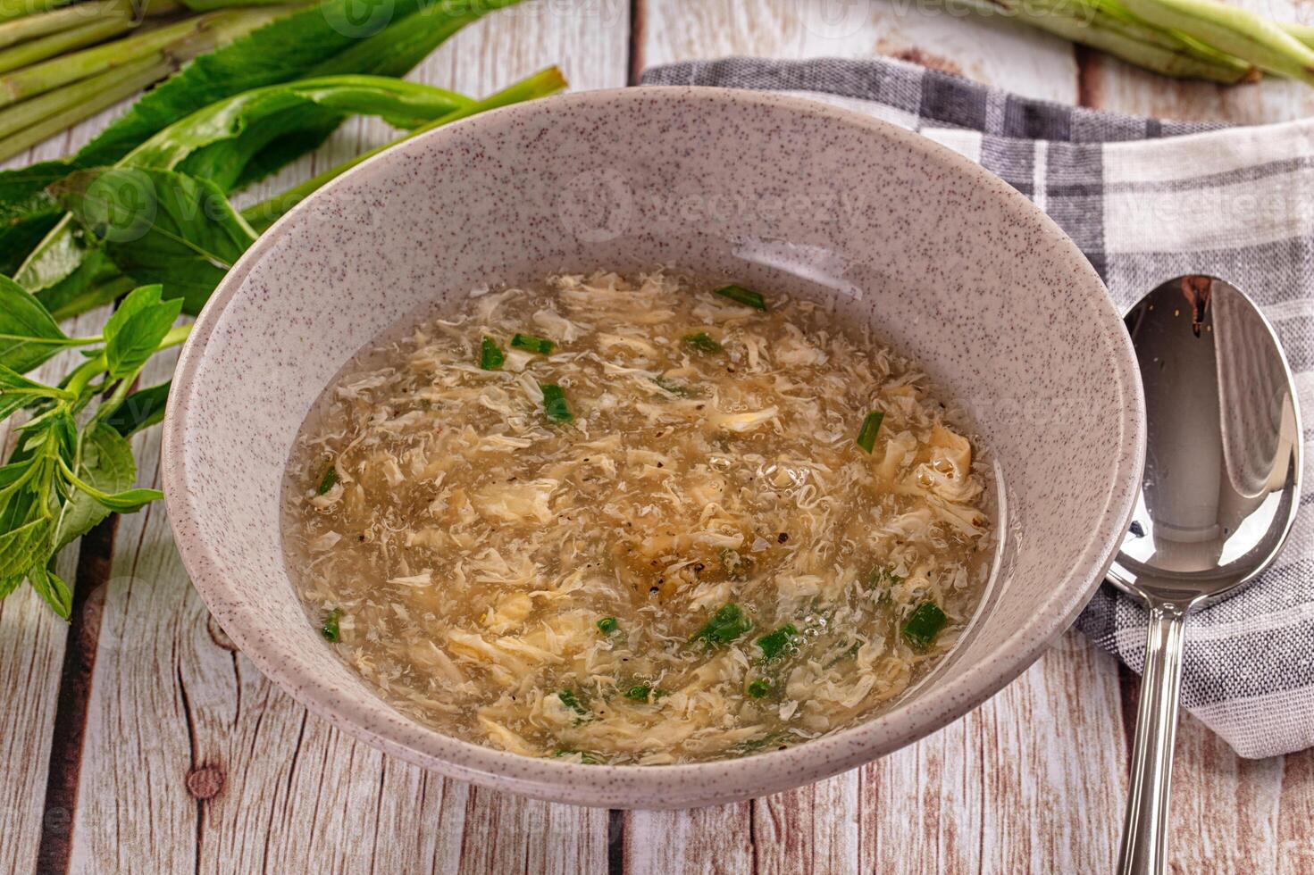 A bowl of soup with a spoon and some green vegetables photo