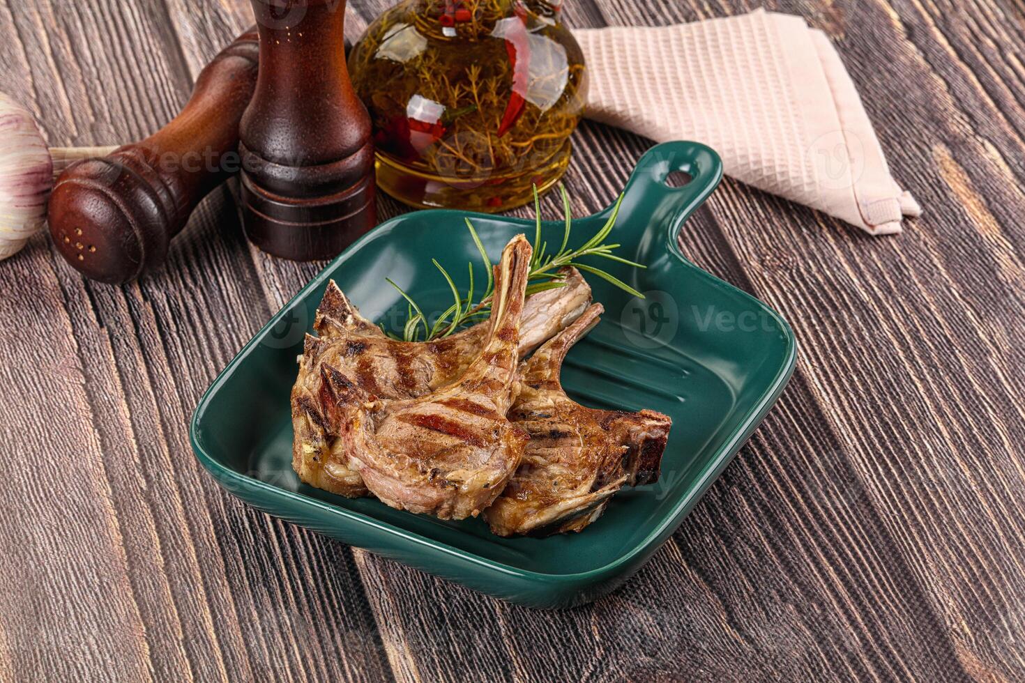 Grilled lamb chops in a green dish on a wooden table photo