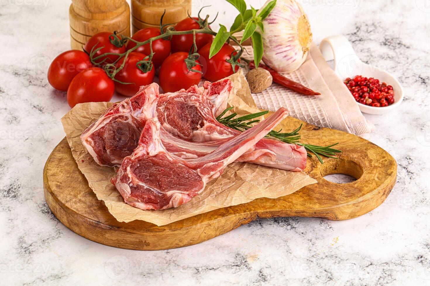 Raw lamb chops on a cutting board with tomatoes and spices photo